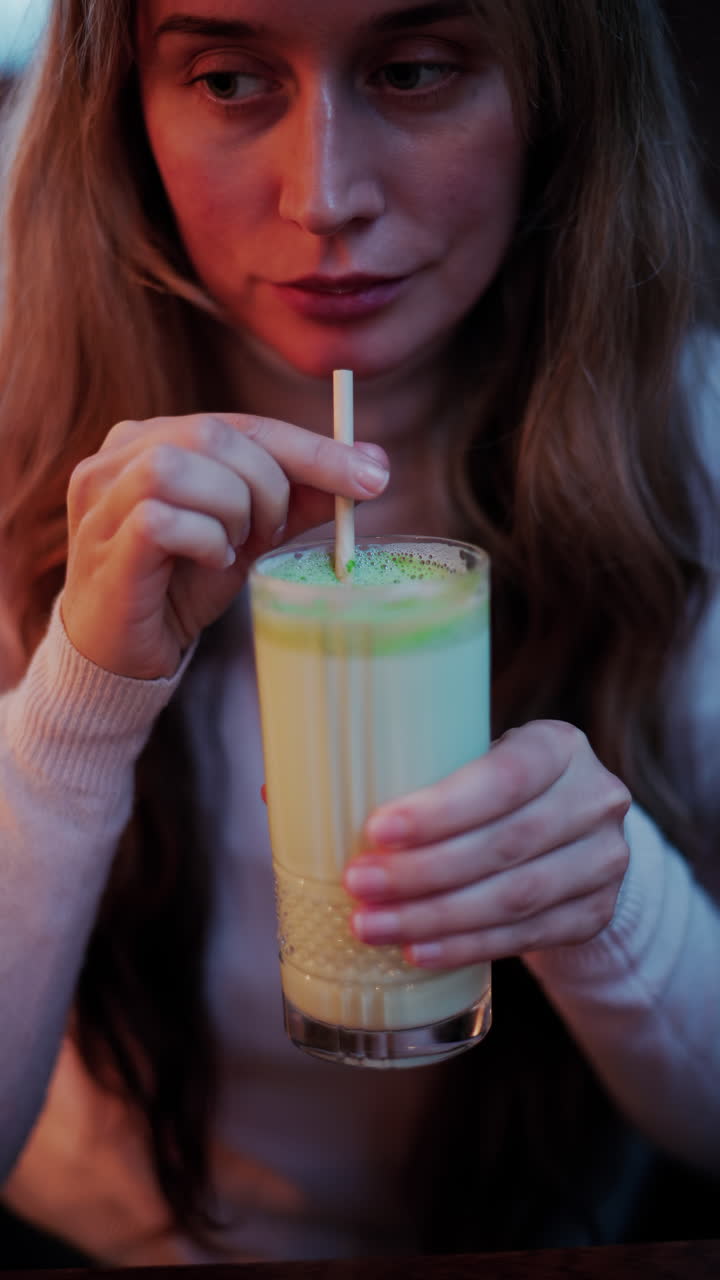Close up of a woman mixing a matcha latte with a paper straw at a cafe. Vertical