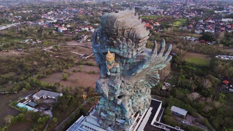 the garuda wisnu kencana sculpture in bali is shown from above in this stunning drone video, with the massive figure of wisnu and garuda highlighted by golden light and framed by tropical scenery