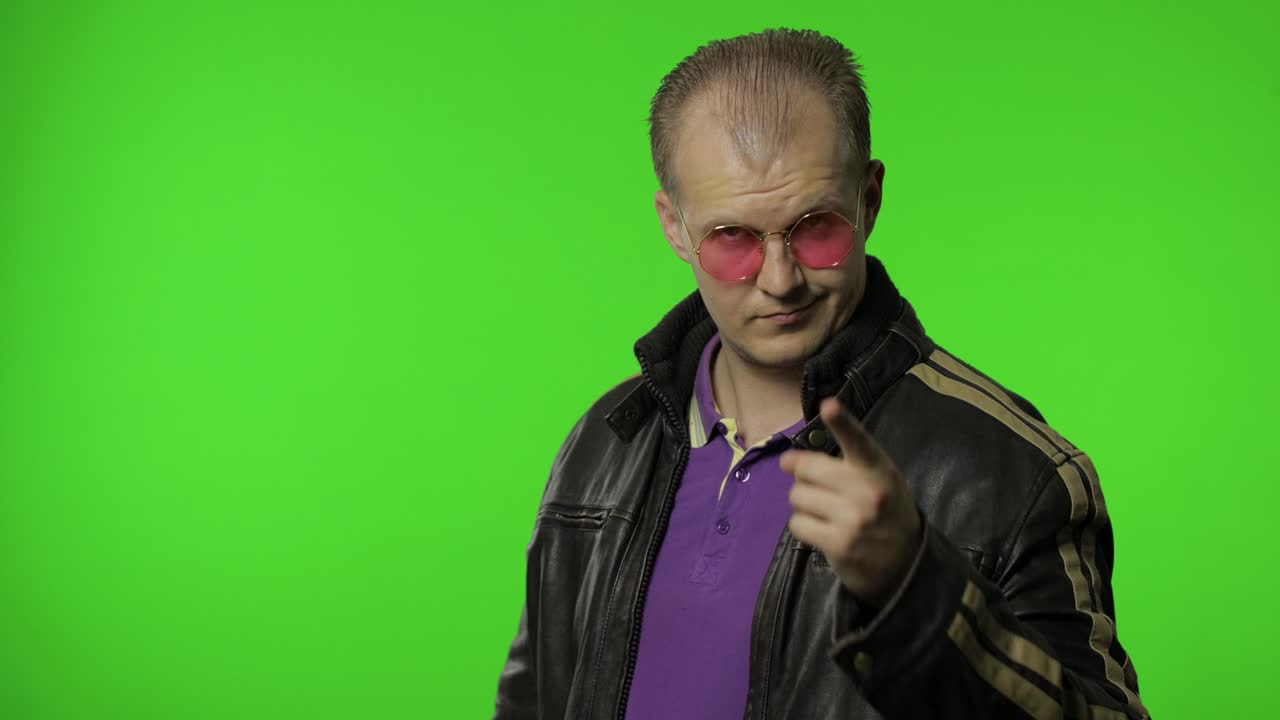 hombre rocker guapo con gafas de sol rosas apuntando con el dedo a usted, mirando a la cámara, haciendo una elección