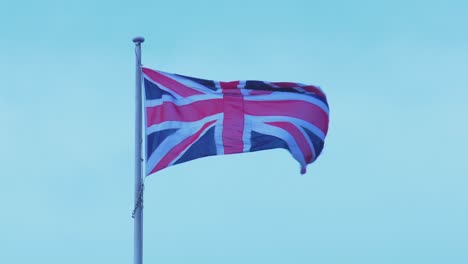 close-up of union jack flag waving in the wind - british flag against light blue sky 4k