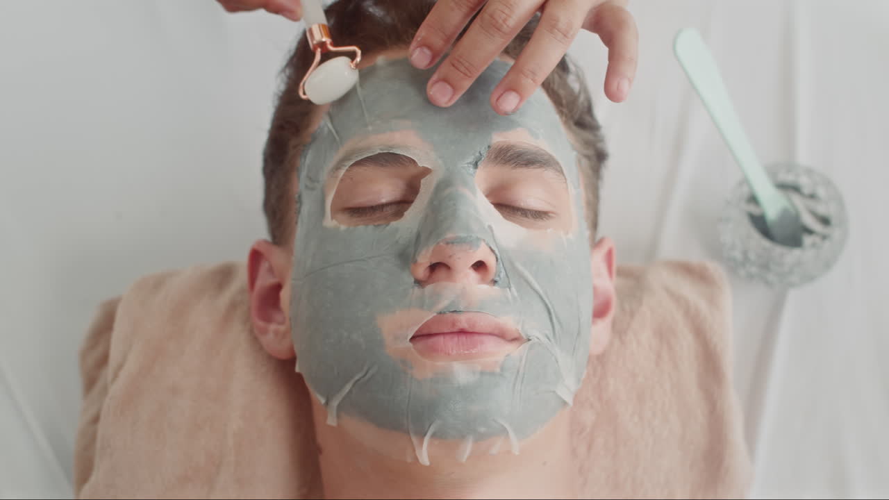 Young Man Getting Facial Procedure with Jade Roller and Masks