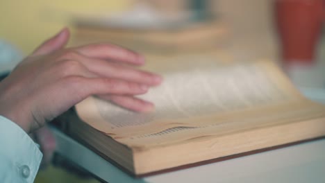 schoolboy turns pages of book at table in light room closeup