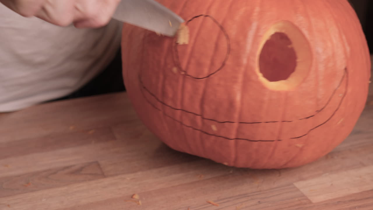 el hombre talló los ojos de cabeza de calabaza con un cuchillo sobre una mesa de madera.