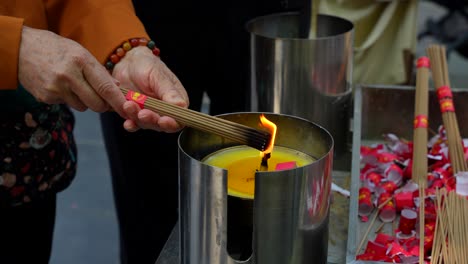 close-up of old female hands lighting incense sticks for prayer and reflection in a chinese temple