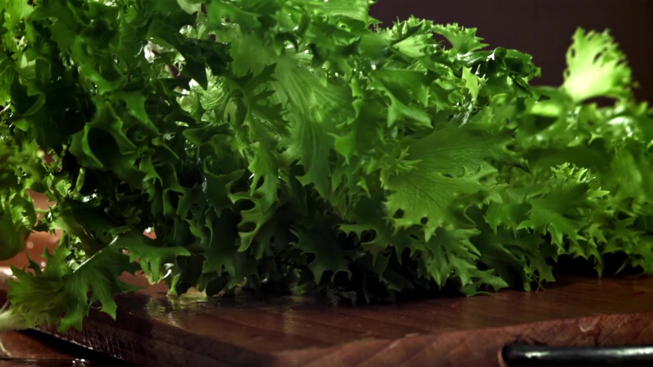 Färsk grön sallad faller ner på en träskärbräda i slow motion.