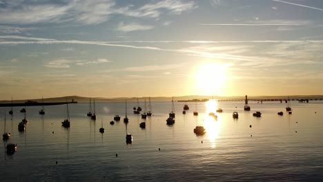 boats silhouetted on golden shimmering harbour ocean surface aerial view slowly circling right