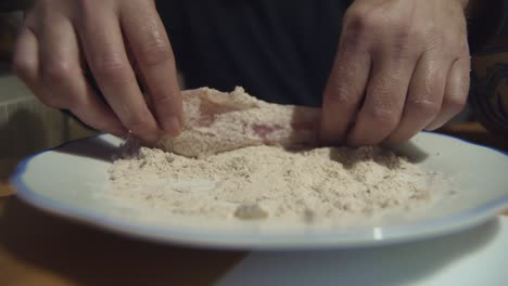 Las-Manos-Cubren-La-Carne-De-Shnitzel-En-Un-Plato-De-Harina-Antes-De-Cocinar,-Primer-Plano