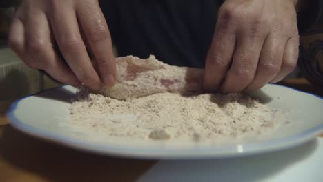 las manos cubren la carne de shnitzel en un plato de harina antes de cocinar, primer plano