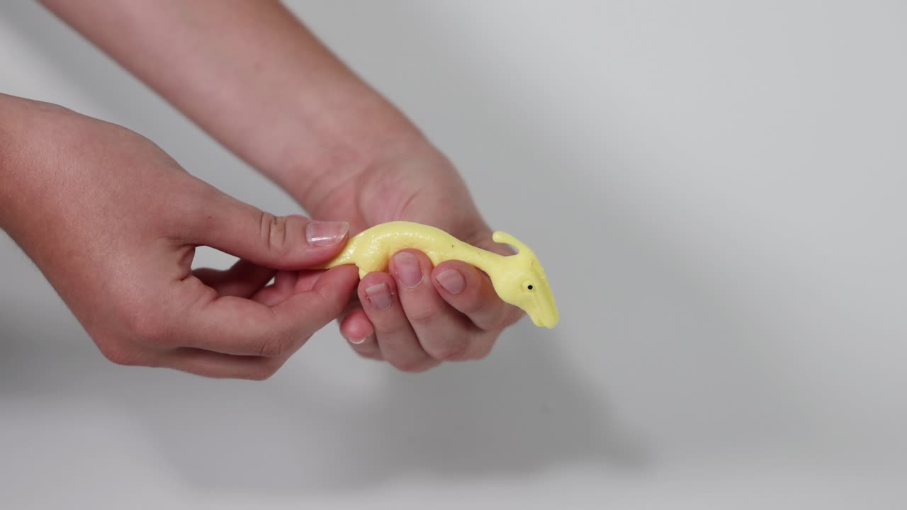 manos aplastando un juguete de dinosaurio amarillo