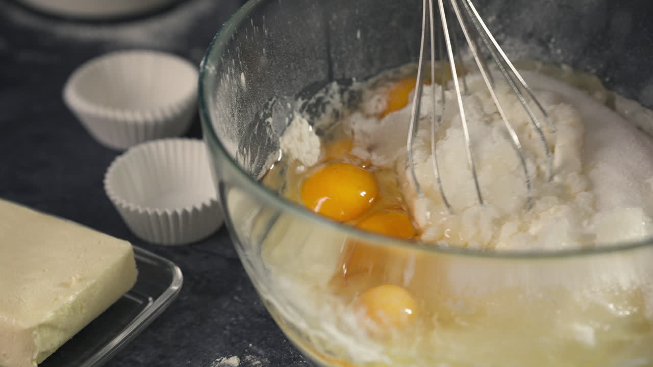 Whisking cupcake batter smoothly as part of the dessert preparation process, metal whisk breaks yolks and combines ingredients