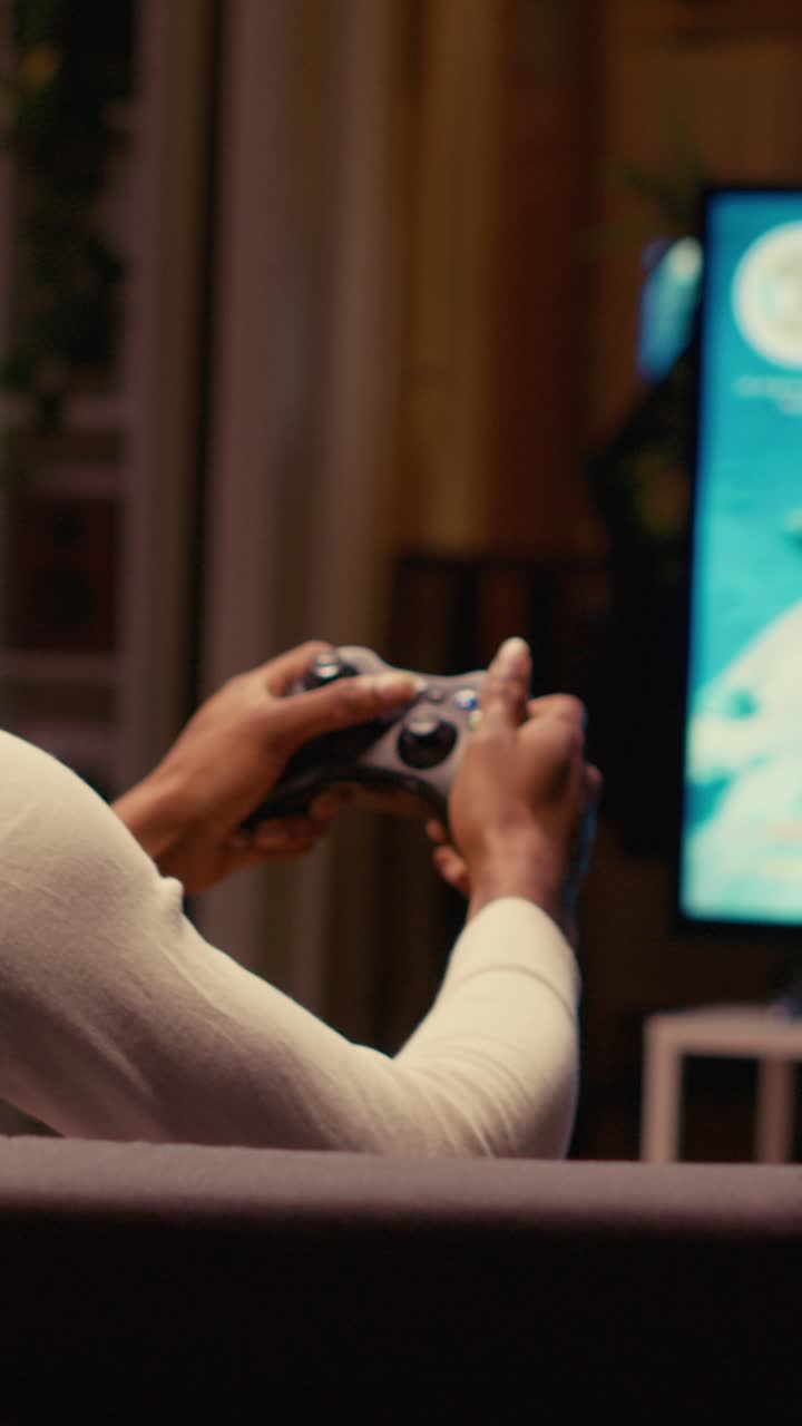 Video verticale. Un uomo gioca con una console ed è felice di aver finalmente completato una missione di un videogioco per giocatore singolo.