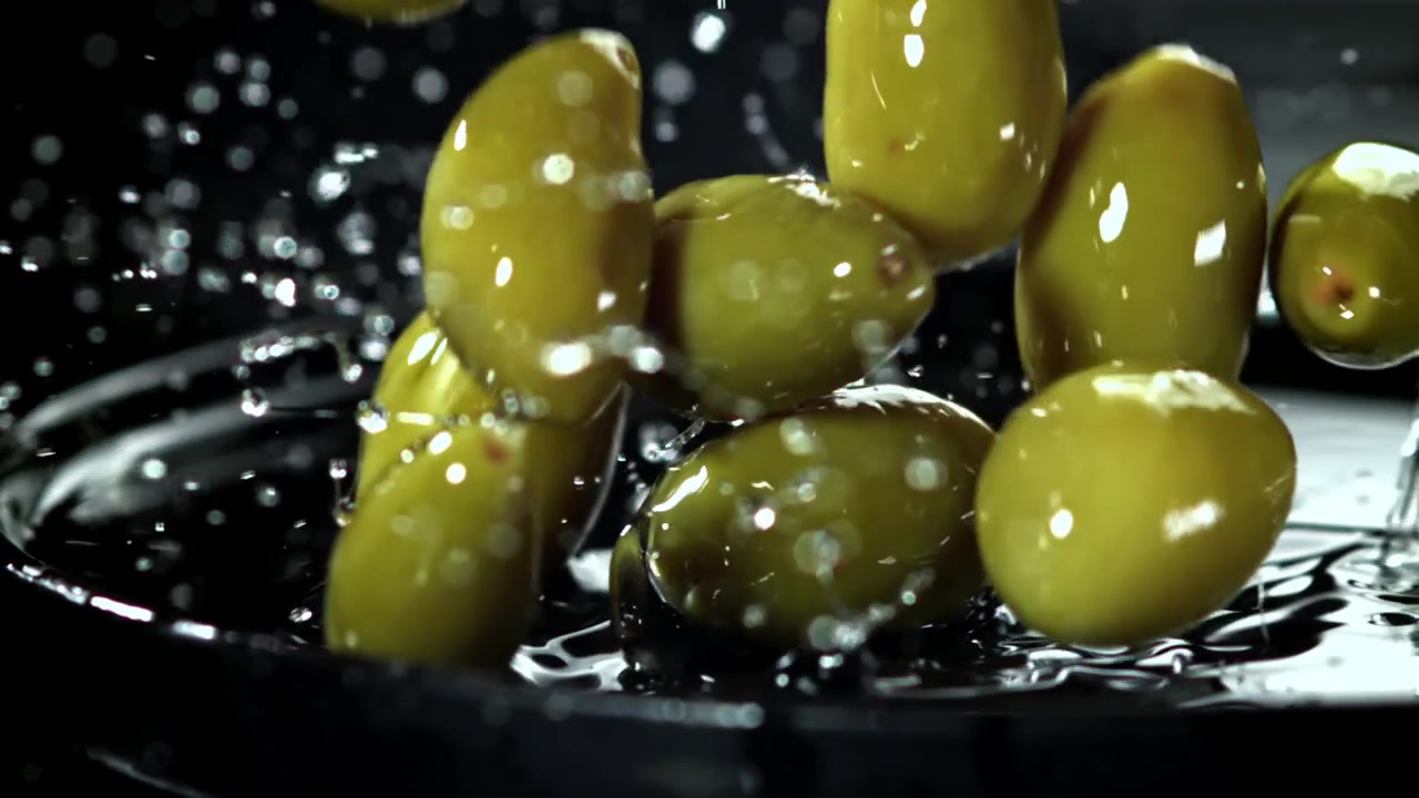 Olive verdi che cadono e schizzano nell'acqua al rallentatore.