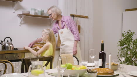 little girl helping her grandmother to set table for dinner and bringing plates