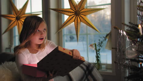zoet jong meisje reageert verbaasd met het openen van een geschenk op kerstmorgen
