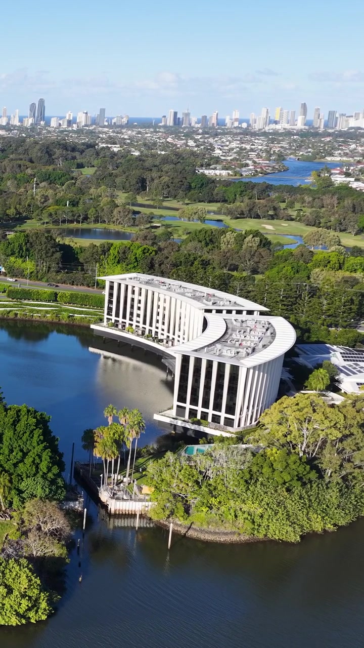 Una ripresa aerea con drone cattura un moderno edificio alberghiero curvo accanto a un lago e alla vegetazione.