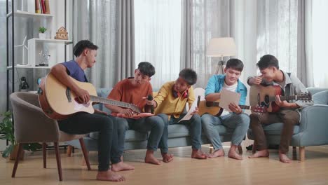Group Of Young Asian Friends With Musical Instruments Helping Each Other Composing Music On The Papers At Home At Home