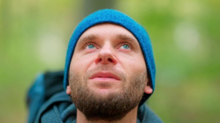 Uomo pensieroso con berretto blu che guarda in alto in una foresta