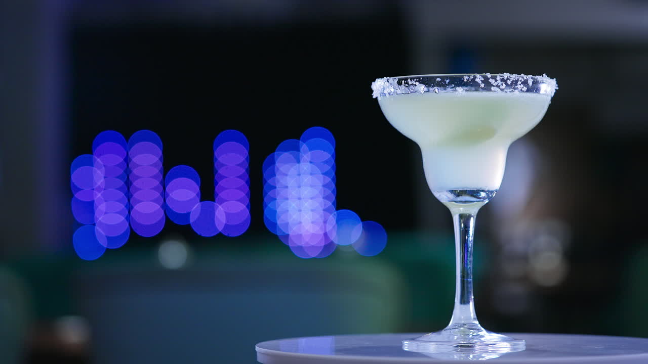 Glass goblet on the little rotating table. Light beverage with a piece of lime inside. Close up. Blurred backdrop.