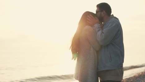 um casal a beijar-se na praia ao pôr do sol.