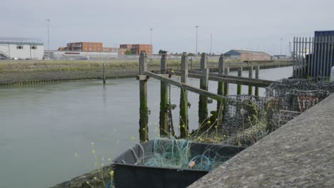 un viejo muelle con postes en descomposición se encuentra en aguas verdosas bajo un cielo gris cerca de edificios industriales y trampas de langosta