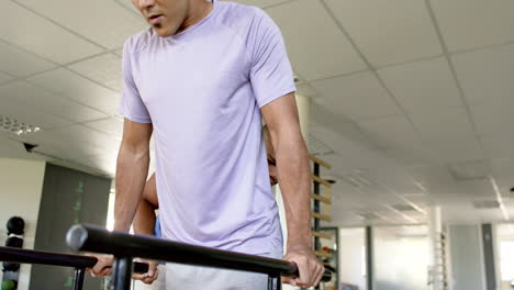 man in rehabilitation, using parallel bars with therapist's assistance in gym