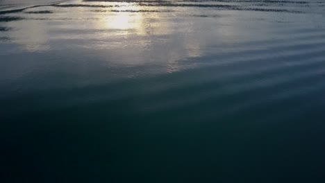 Aerial-tracking-shot-above-turquoise-waters-towards-sunrise-behind-calm-fishing-village-in-the-Philippines