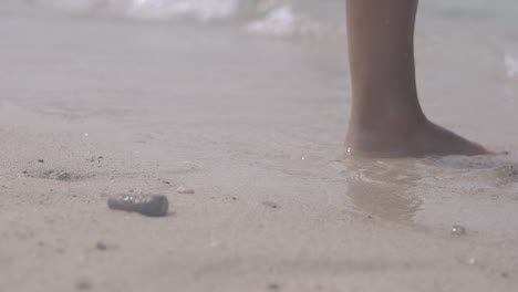 woman with red pedicure walks on beach and enjoys waves