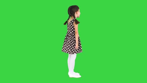 cute little girl in polka dot dress talking about something to the camera on a green screen, chroma key