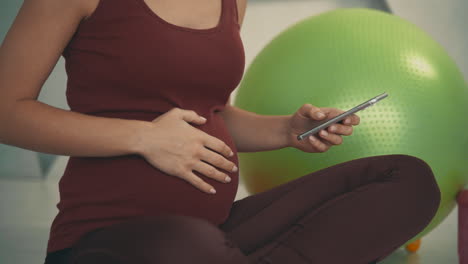 pregnant athlete female using her phone at home. close-up. pregnancy and motherhood.