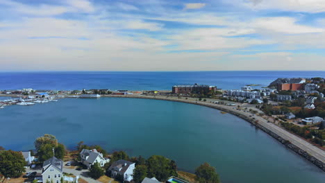 Drone-view-of-a-partly-sunny-sky-overlooking-Hull-Bay,-Nantasket-Beach,-Hull,-MA-USA-and-the-Atlantic-Ocean-while-cars-drive-on-a-shoreline-motorway