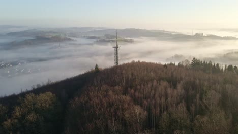 Observation-tower-with-transmission-mast-at-sunrise-sitting-on-the-edge-of-a-steep-hill-in-Morsbach,-Germany