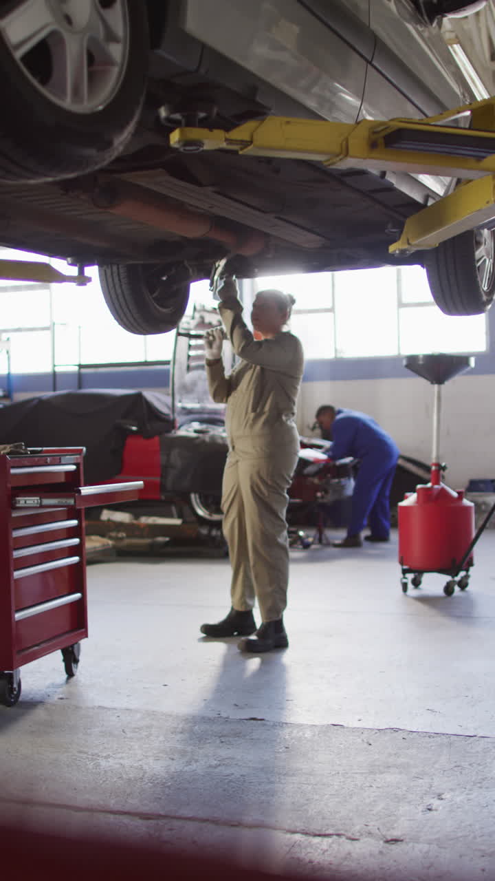 video vertical de una mecánica de automóviles biracial usando una tableta y comprobando el coche