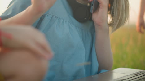 a close-up shot of a woman's hand in a blue gown as she types on a laptop while sitting on a grassy area. the scene captures a gentle moment as she stops a child's hand from pressing the keyboard