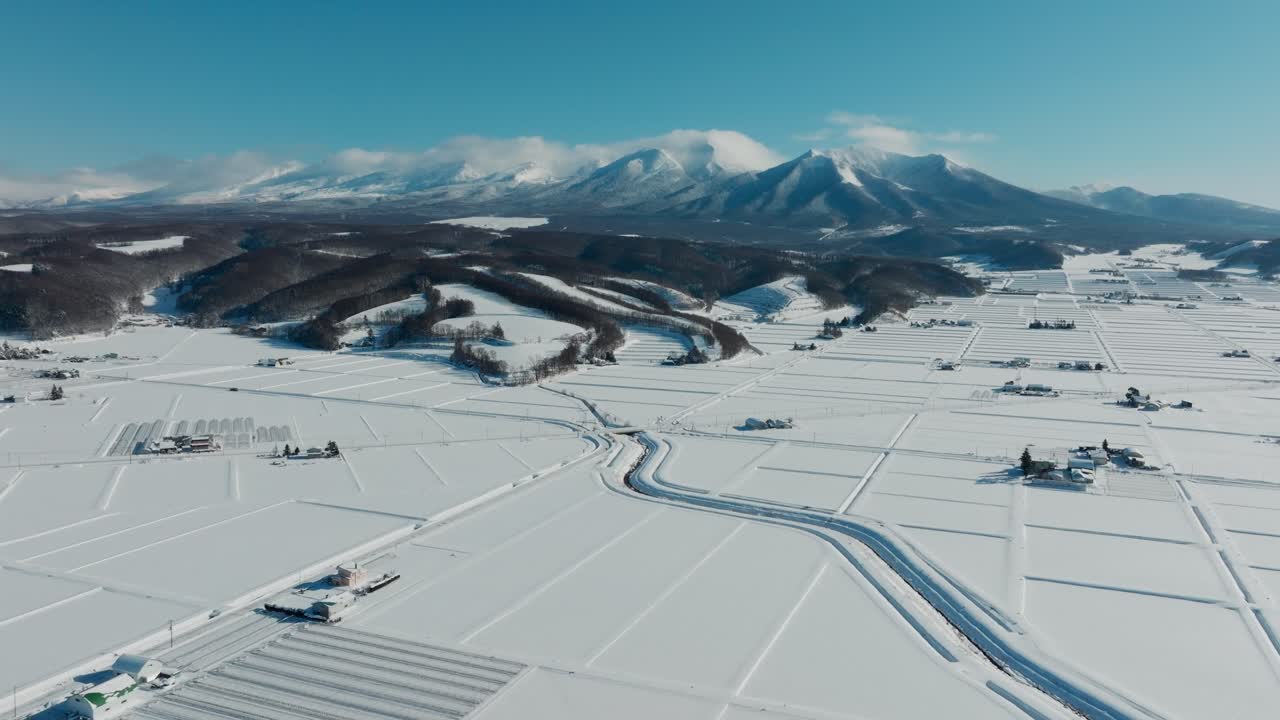 Snow-covered Farmland In Town Of Nakafurano In Tokachi Mountain Range In Background. Kamikawa, Hokkaido, Japan. wide aerial shot