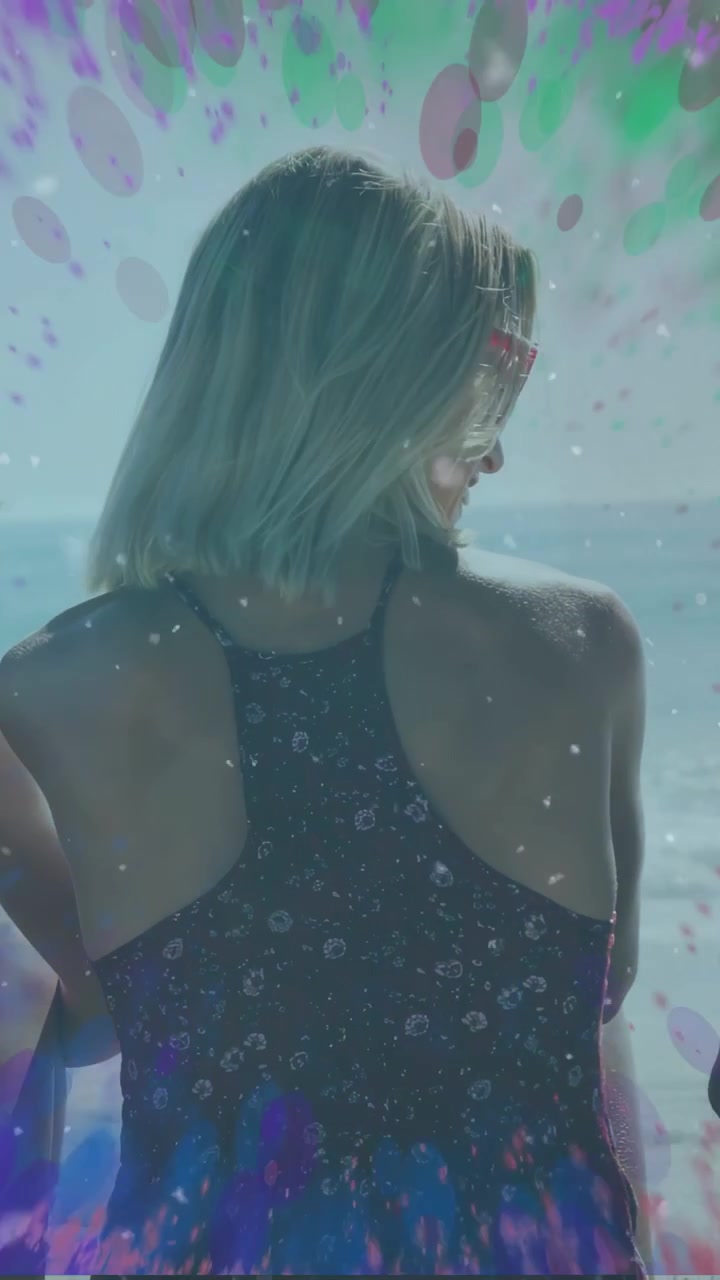 Video verticale: Donna che si gira verso il mare, il vento solleva occhiali da sole rosa, anelli che pulsano, mentre guarda il mare, viaggio