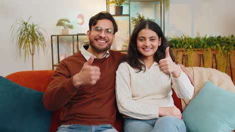 smiling young indian family couple man woman sitting showing thumbs up giving approval good feedback