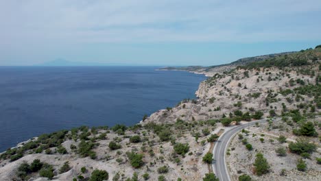 Aerial-View-Of-A-Coastal-Road-With-High-Cliffs,-Clear-Blue-Sky-And-The-Mediterranean-Sea-in-The-Background,-Thassos,-Greece