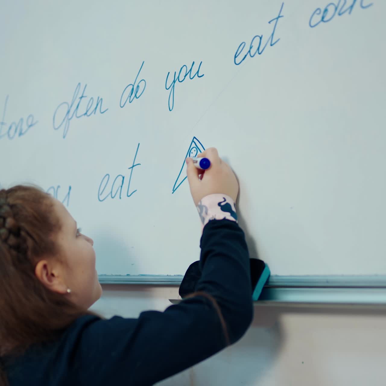 Schoolgirl writing on a blackboard. Side little girl in a school uniform writes with a marker on white magnetic board at primary school.