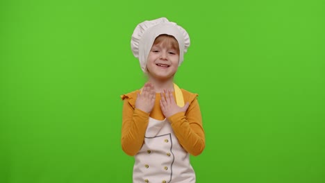 a young girl dressed as a chef smiles and claps her hands in front of a green screen