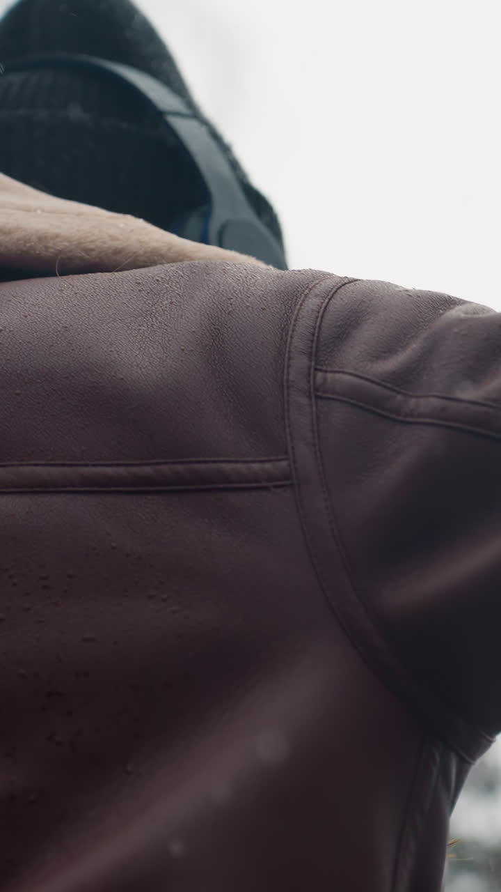 Back shot of lady wearing black knit cap, brown shearling jacket with arms outstretched, walking joyfully outdoors on cool autumn day, embracing nature and enjoying fresh air in a peaceful setting