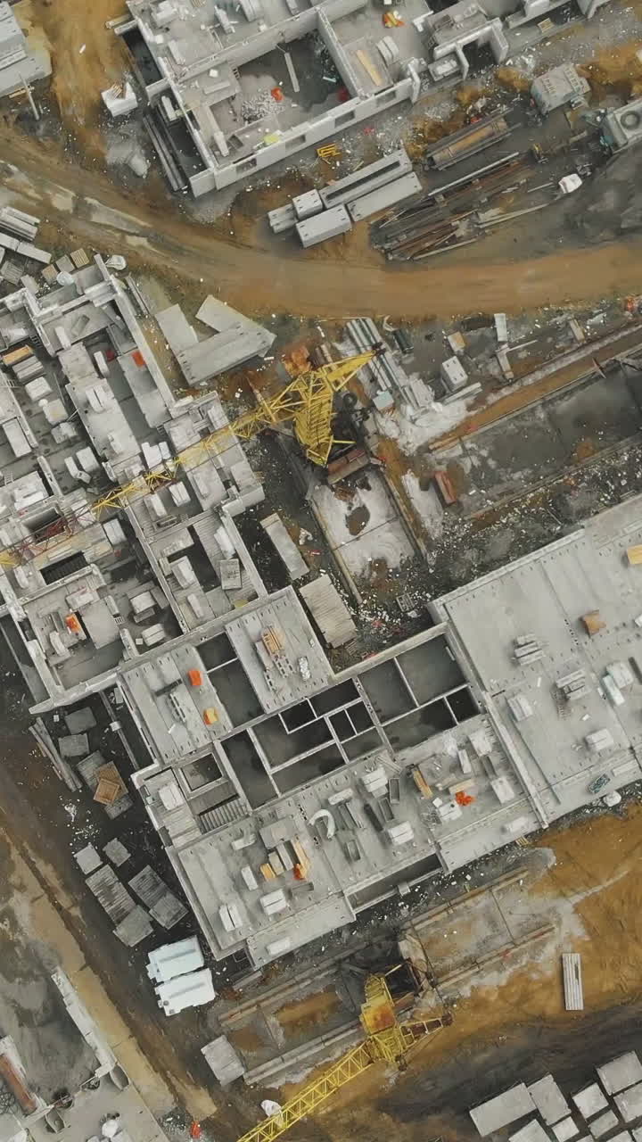 large construction site with buildings under development and high yellow construction cranes vertical bird eye view