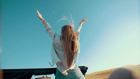 back view of girl standing in convertible with her hands up against sky. happy woman standing in convertible, enjoying life, view from back