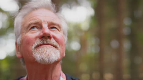 active retired senior man walking in woodland countryside wearing backpack