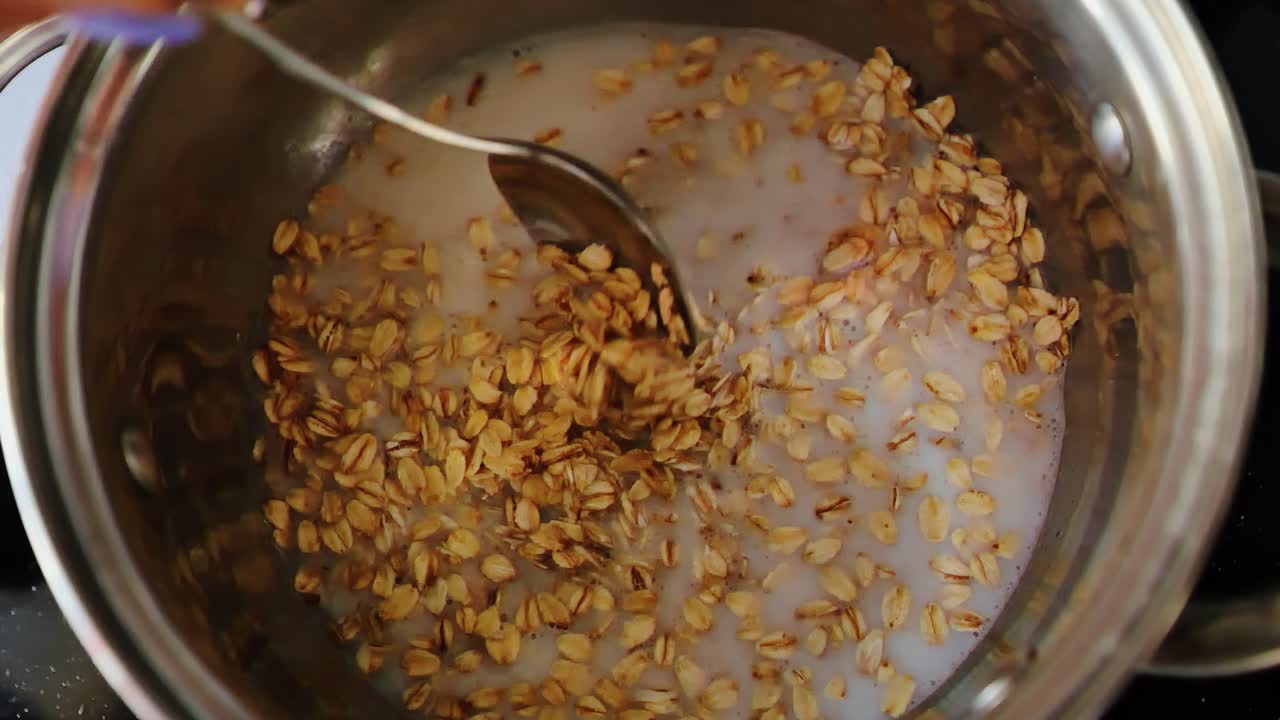 Soft oats swirl as spoon stirs warm water, milk blend during gentle slow motion
