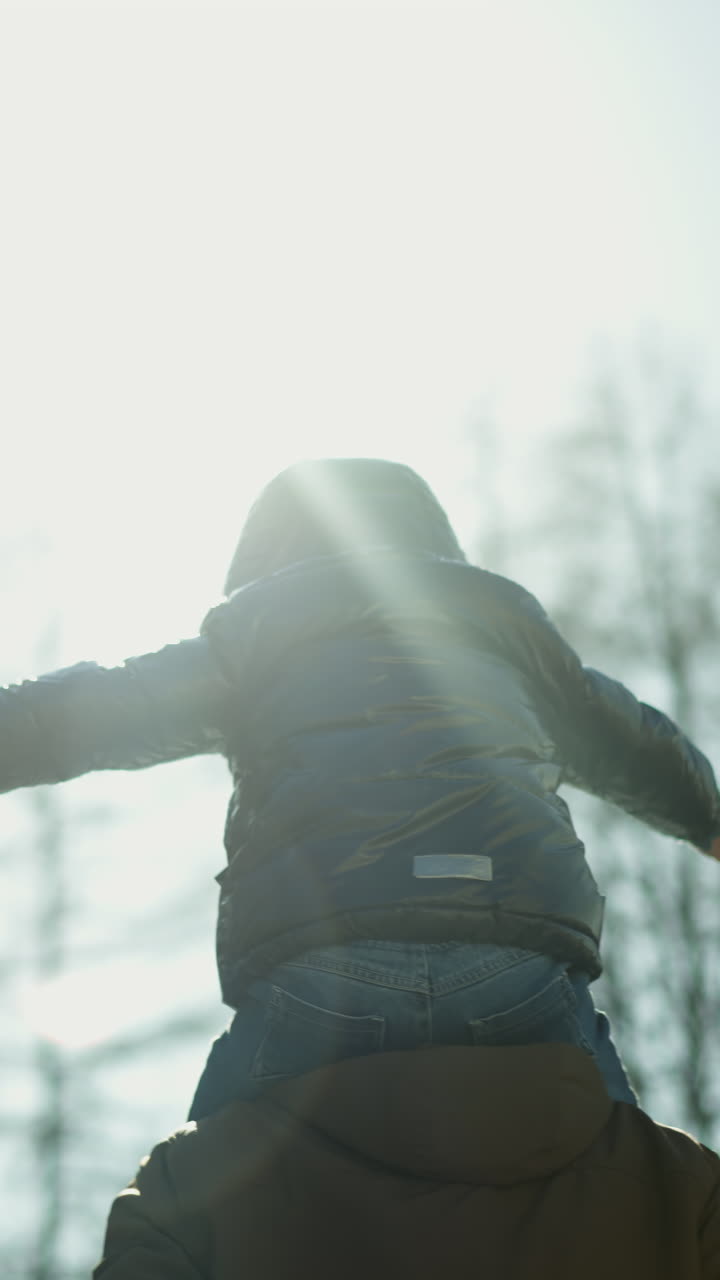 한 아버지가 그의 아들을 어깨에 고 나무로 둘러싸인 길을 걸어가는 동안, 아이는 조심스럽게 보이면서 팔을 넓게 펴고, 빛이 반사되는 동안