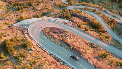 aerial view following a longboard rider on a countryside road with a series of sharp hairpin bends, bright sunlight