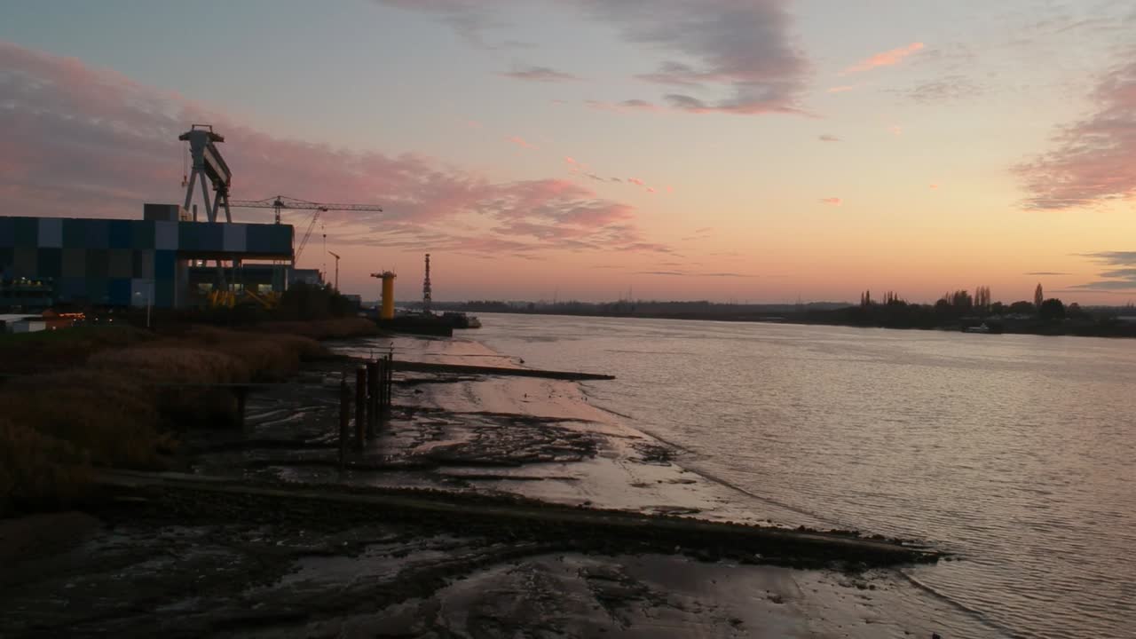Bakåtriktad flygvy över industribyggnader vid floden Schelde efter solnedgången