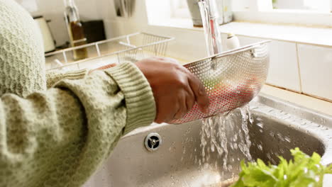 Hands-of-african-american-senior-woman-washing-tomatoes-in-sunny-kitchen,-slow-motion