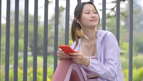 4k young asian woman listening to music from earphones and smartphone while jogging at public park the city in the morning.