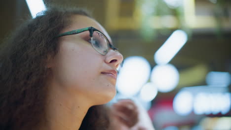 close-up profile of woman wearing glasses, adjusting hair with serene expression, soft bokeh lights and blurred background providing gentle ambiance, highlighting a reflective moment